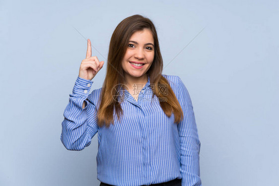 年轻女孩在孤立的蓝色墙上展示并举起一只手指在图片