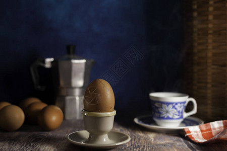 深蓝色背景的木桌上的鸡蛋杯里的熟鸡蛋新鲜的生鸡蛋一杯咖啡咖啡背景图片