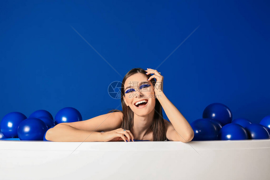蓝底浴缸里有气球的时尚年轻女子肖像蓝色背图片