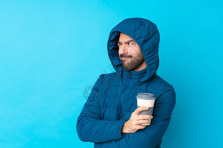 穿着冬季夹克和咖啡的男子在孤立的蓝色背景画像上图片