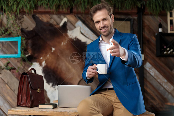 一位愉快的商人向前指头并举着咖啡杯图片