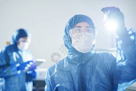 身着蓝色生物危害服和安全护目镜的严肃沉思亚洲学家站在科学实验室研究图片