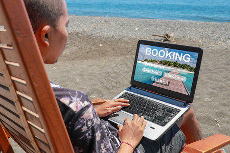 旅行预订概念旅游旅馆和网上订票年轻人在海滩上用黑色火山沙子做笔背景图片