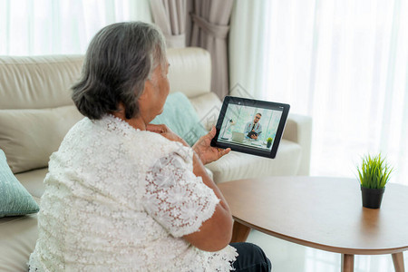 老年妇女在家时在数字平板电脑在线医疗数字技术服务咨询上感觉喉咙痛图片