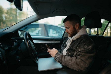 一个留着胡子的男人在舒适的车里用智能手机在网上做生意背景图片