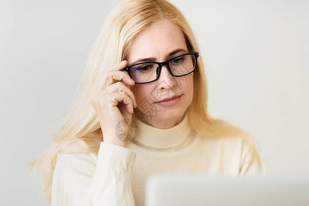 视力问题中年妇女透过笔记本电脑的眼镜看望图片