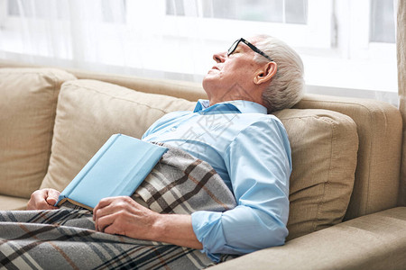 老人志愿活动疲惫的老人在沙发上打着格子打盹背景