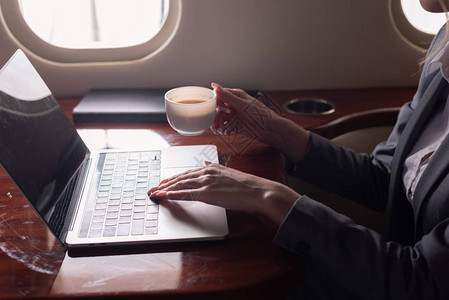 商业女商人持有咖啡杯并在出差途中在飞机上用笔记本电图片
