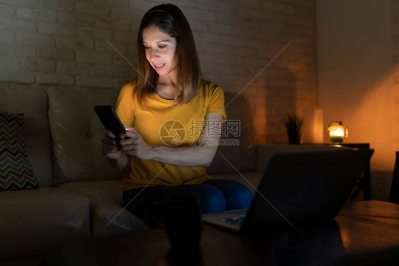 白人可爱女使用笔记本电脑和智能手机在家中检查晚间图片