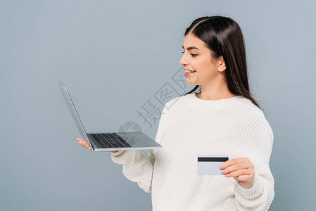 穿着白色毛衣的漂亮女孩拿着笔记本电脑和信用卡在图片