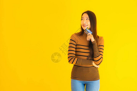 肖像美丽的亚洲年轻女使用智能手机或带信用卡的手机在黄色孤立背景下图片