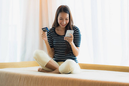 使用带信用卡的手机或智能手机在客厅区的沙发上购物的美丽亚洲图片