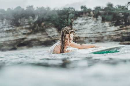 美丽的女人在冲浪板上海洋中的美丽女孩在雨中冲浪湿头发和喷雾女孩从水中出现穿着白色比基尼图片