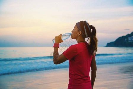 亚洲妇女早上在海滩上慢跑锻炼您可以在海边散步和用塑料瓶喝水来放松身心海滩运动锻炼图片