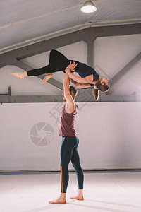 杂技瑜伽和瑜伽姿势的主题一对两男一女站在体位的置那家伙用伸出的手臂把女孩高地拱起来在有工作室背图片