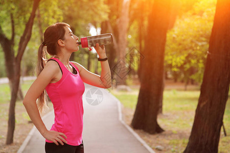 美丽的运动员跑者女子在公园饮用水图片