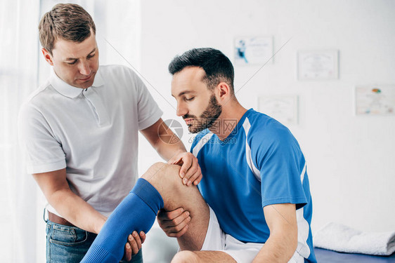 英俊足球运动员在医院的腿部按摩治疗图片