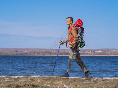 一个带着假肢的人在河边行走的侧面图背着包的北欧行走积极的生活方式动图片
