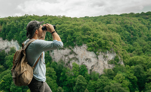 一名男子背着包站在高处使用双筒望远镜检查森林环境研图片