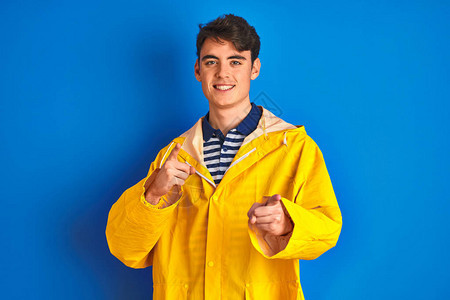 身穿黄色雨衣的青少年渔夫在孤立的背景中用笑脸和笑脸对着镜头指手脚图片