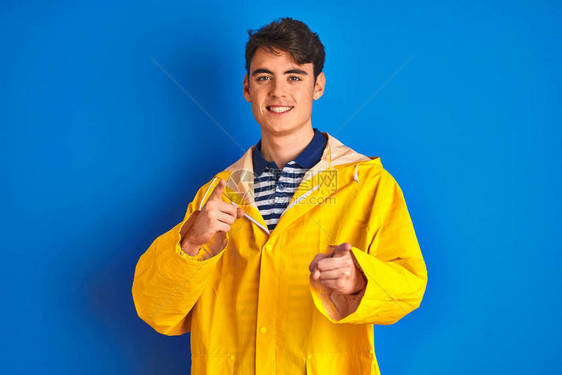 身穿黄色雨衣的青少年渔夫在孤立的背景中用笑脸和笑脸对着镜头指手脚图片