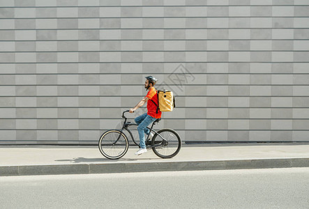 骑自行车的送货员留着胡须和大背包的年轻人在灰色砖墙背景侧视图自由空间的城背景图片