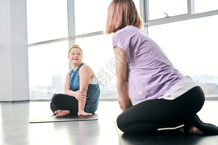 穿着运动服的快乐残疾女孩一边坐在垫子上一边看着她的朋友图片