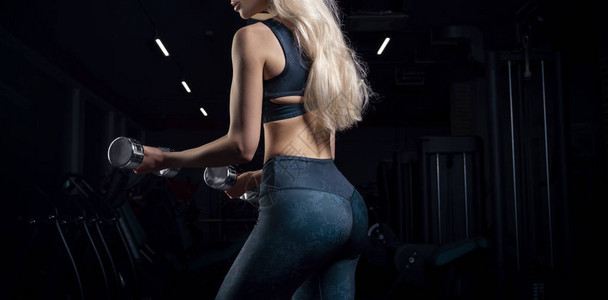 迷人的女运动员在健身房里用哑铃摆姿势健美健身伸展健康饮食的概图片