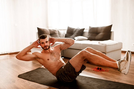 年轻人在家参加体育运动t恤赤膊男运动员在瑜伽垫上锻炼腹肌的照片锻炼身体的大一新生在阳光明媚的公图片