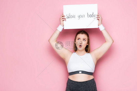 超重过度兴奋的女孩拿着标语牌爱着你的身体在粉红色的头图片
