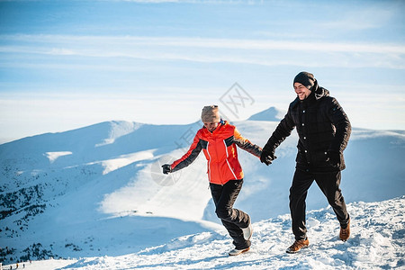 幸福的情侣穿着温暖的衣服手牵跑在山上在阳光图片