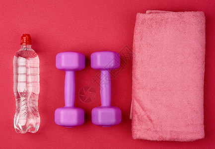 一对紫色塑料哑铃和红新胎垫上的粉红色毛巾图片