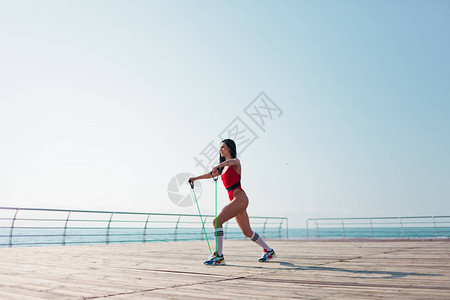 穿红色运动健身服的年轻体操女子在早晨沙滩上做有氧锻炼和放大图片