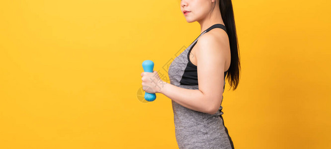 穿着运动服的笑脸亚裔妇女用浅橙色背景的蓝色哑铃抽筋肌肉健康生活方式图片