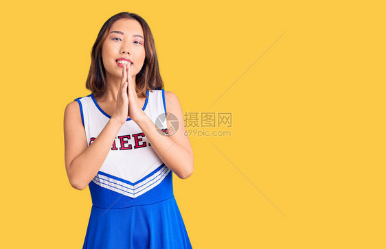 身穿啦队员制服的年轻女孩用双手一起祈祷祈求宽恕微笑着满图片