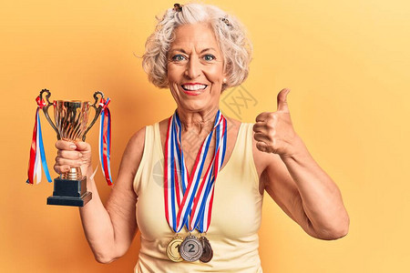 身着奖牌的高级灰色头发女子持有冠军奖杯图片