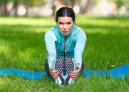 女人在慢跑前热身肌肉坐在城市公园的草地上伸展肌肉图片