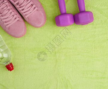 紫色哑铃和干净的塑料水瓶绿色毛巾上的粉色鞋顶部视野平板图片