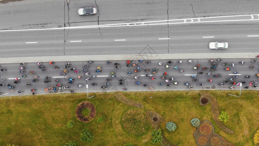相机缩小了沿着柏油路骑行的业余自行车马拉松经过超速行驶的汽车和绿色图片