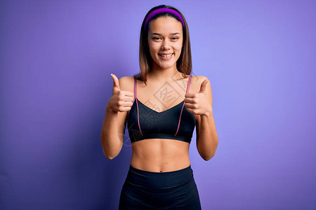 年轻漂亮的运动型女孩在孤立的紫色背景成功标志上穿着运动服做运动图片