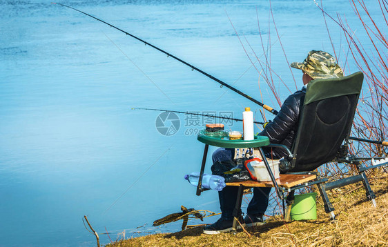 渔夫坐在沙滩上的椅子上拿着钓鱼竿和鱼图片