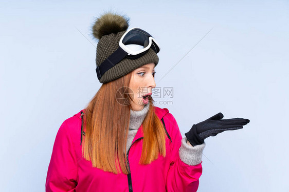 穿着滑雪眼镜的雪花红头发女人在隔绝的蓝色墙上挂着棕榈上想图片