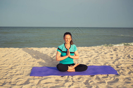 身材苗条的黑发女人坐在美丽阳光明媚的多风海滩的运动垫上图片