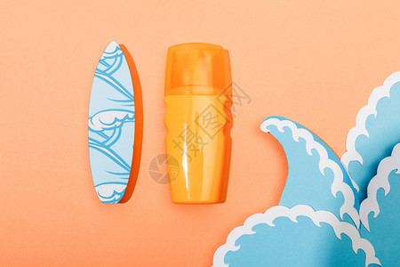 涂有纸切割海浪和橙色背景冲浪板的防晒霜喷图片