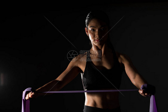 亚洲苗条健身女锻炼伸展腿手臂阻力带在雾烟黑暗背景低曝光环境图片
