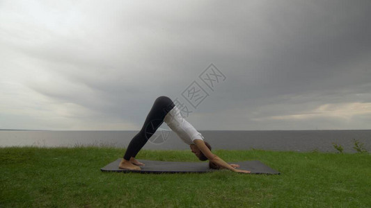 年轻健康的女人在湖或海附近的海岸上练习瑜伽女人做向下图片