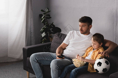 父亲和儿子在足球旁看电视喝图片