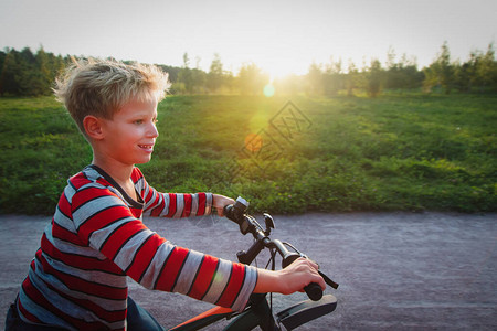 快乐的可爱男孩在日落自然中享受骑自行车图片