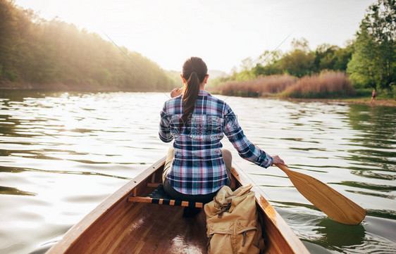 划着木独舟旅行女孩在日落湖上划独木舟的后视图皮划艇独木图片