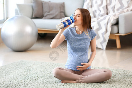 美丽的孕妇在家训练期间喝水图片